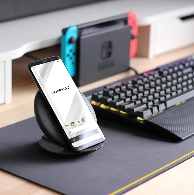 Smartphone on a stand with a desk setup including a keyboard and gaming console.
